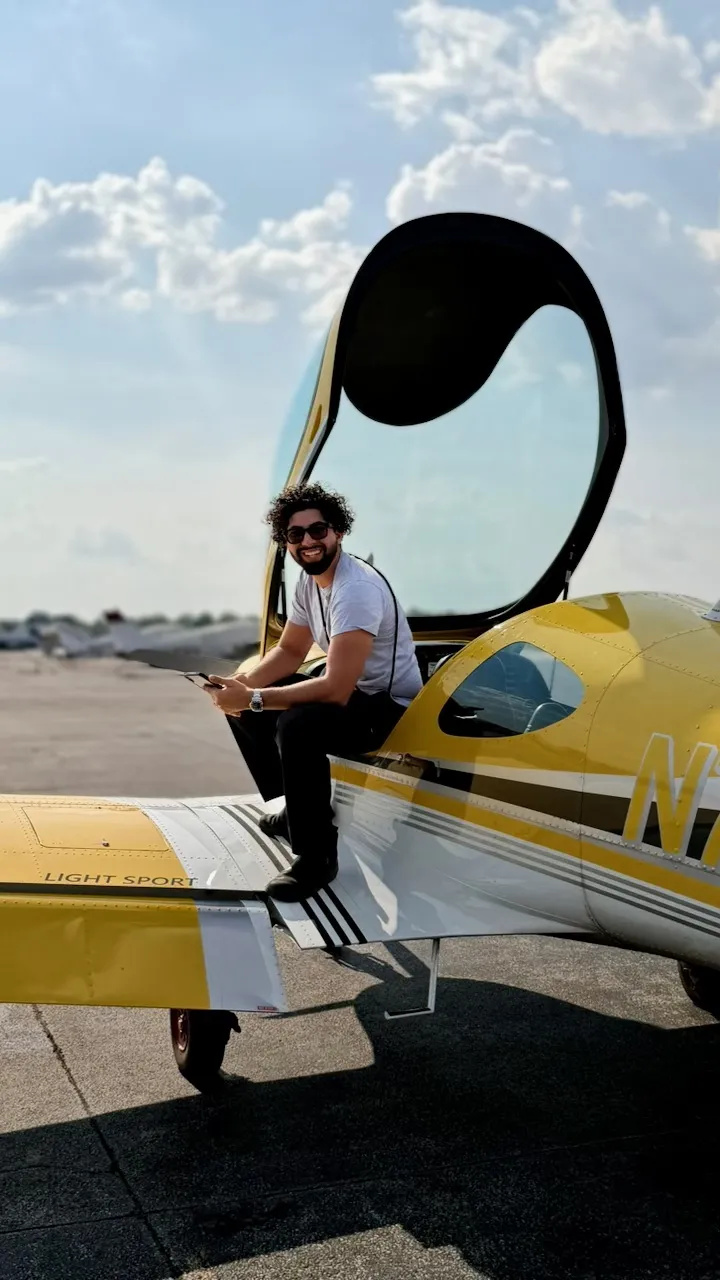 Diego Suarez, FAA flight instructor, sitting on the wing of a light-sport training airplane with the canopy open at Bowman Field